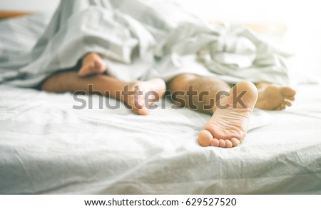 Close up of male and female feet on a bed - Loving couple having sex under white sheets in the bedroom - Concept of sensual and intimate moment of lovers - Vintage filter - Focus on male foot