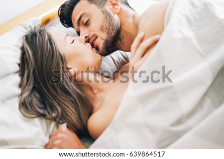 Young couple in love kissing in a bed under white blanket - Passionate lovers having romantic and intimate moments on the bed - Sex and passion concept - Focus on male face