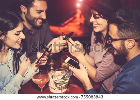 Happy friends using mobile phone and having fun with cocktails in a jazz bar - Young people addicted to new smartphone technology - Concept of youth, cellphone and lifestyle - Focus on right male hand