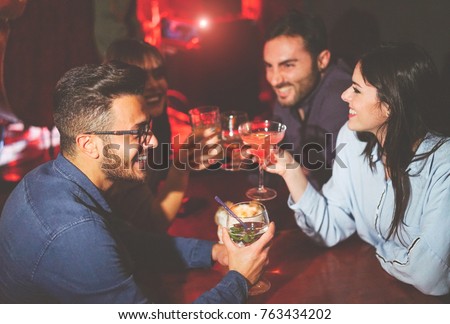 Happy friends drinking and toasting cocktails in a jazz bar - Young people cheering and laughing together in a club at night - Friendship, lifestyle, nightlife concept