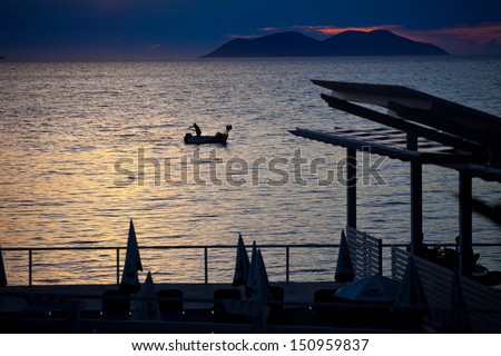 Fisherman in a boat with net is his hand in the sunset, in Albania
