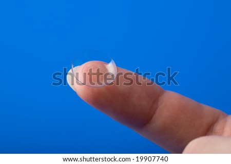 finger holding contact lens over blue background