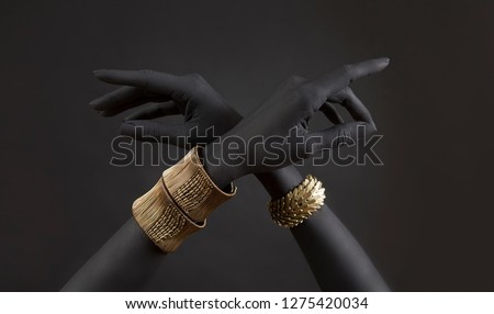 Black woman\'s hands with gold jewelry. Oriental Bracelets on a black painted hand. Gold Jewelry and luxury accessories on black background closeup. High Fashion art concept