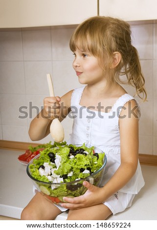 Child girl preparing greek salad, little girl preparing and eating vegetable salad