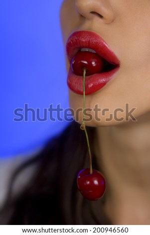 Sexy woman eating Cherry. Sensual Red Lips on a blue background
