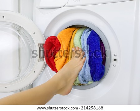 woman loading colorful laundry (clothes) in the washing machine
