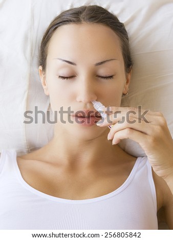 Medicine ayurvedic spray nasal. Sick young woman using nasal spray and laying on sofa