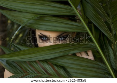 Sexy beautiful woman hiding behind the palm leaves like a panther in the in the tropical forest in India. Portrait of beautiful caucasian stylish young woman with smokey eyes, wildness