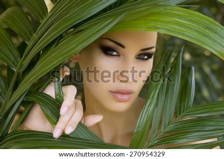 Makeup. Sexy beautiful woman hiding behind the palm leaves like a panther in the tropical forest in India. Portrait of beautiful caucasian stylish young woman with smokey eyes, wildness