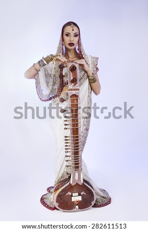 Beautiful Young Indian Woman in Traditional Sari Clothing with oriental jewelry, Bridal Makeup Posing with Sitar. Beautiful Bollywood Girl full height. Eastern fairy tale  (blue lens effect)