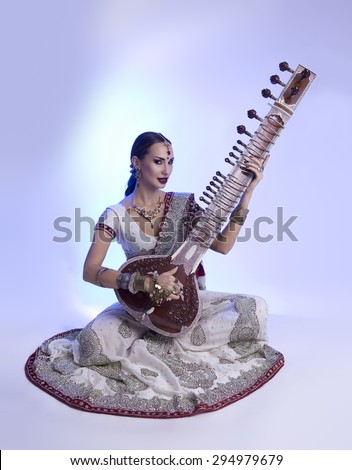 Beautiful Young Indian Woman in Traditional Sari Clothing with oriental jewelry, Bridal Makeup Playing the Sitar. Beautiful Bollywood Girl. Eastern fairy tale  (blue lens effect)