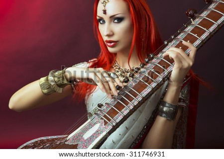 Beautiful Young Redhead Sexy Woman in Traditional Indian Sari Clothing with Oriental Jewelry and Bridal Makeup Playing Raga the Sitar. Beautiful hot Bollywood Girl. Eastern Music