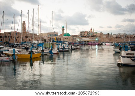 ACRE, ISRAEL - JULY 17, 2014: Local fishing boats, yachts with and nearby monuments, at sunset in the fishing harbor in the old city of Acre, Israel. Acre was a major harbor city for many centuries