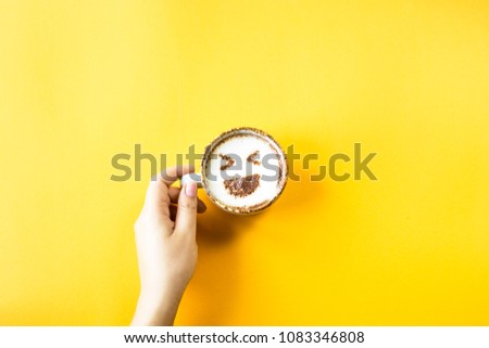A female hand holds a cup of coffee on which is drawn emoji laughter. Emotions in social networks concept. Top view, flat lay
