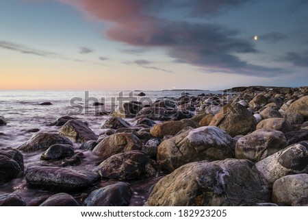 Blinking lighthouse at sunset with iced stones in the foreground.