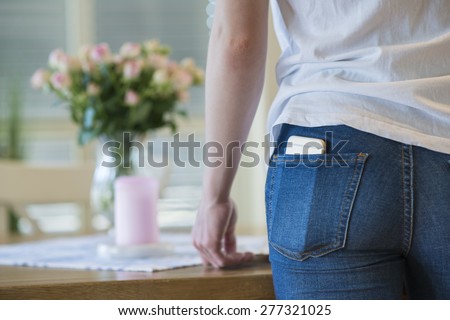Close-up of a girl in white t-shirt and blue jeans with a cell or mobile phone in her back pocket.
