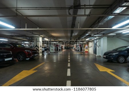 Illuminated underground car parking interior under modern mall with lots of vehicles and arrows on floor, toned