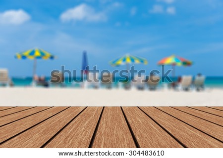 Blurred beach chairs and umbrellas blue sea & sky background with empty wooden deck table ready for product display montage.
