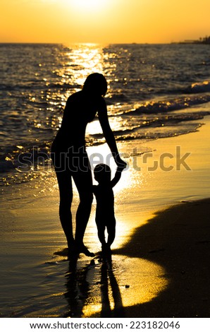 Silhouette mother leads the child\'s hands in the sunset by the sea
