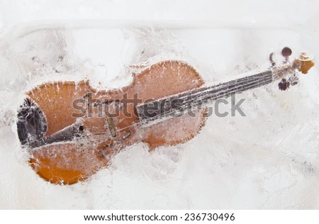 Violin with broken strings frozen into the ice. Close-up.