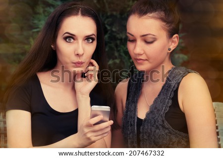 Young Women Surprised by Text Message - Two girls look surprised by something on the smart phone screen.
