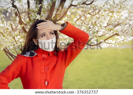 Woman with Allergy with Respirator Mask in Spring Blooming Decor - Portrait of an allergic woman surrounded by seasonal flowers wearing a protective mask