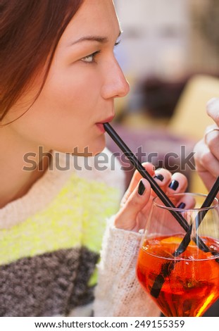 Young woman enjoying a orange drink - spritz - on a sunny day.