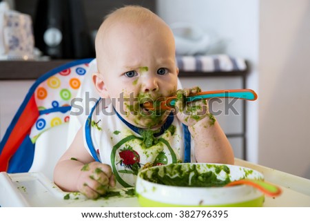 Feeding. Adorable baby child eating with a spoon in high chair. Baby\'s first solid food