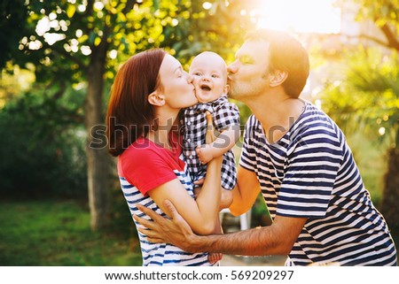 Happy family having fun and laughing on a spring summer day at sunset. Mother, Father and Cute Little Baby Child at stylish casual clothing on nature. Parents and activity with baby outdoors.