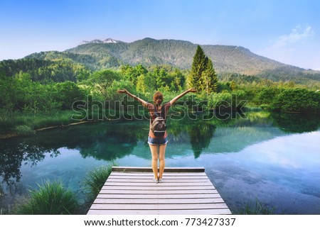 Young woman stands on a wooden bridge with raised arms up on the nature background. Travel, Freedom, Lifestyle concept. Slovenia, Europe.
