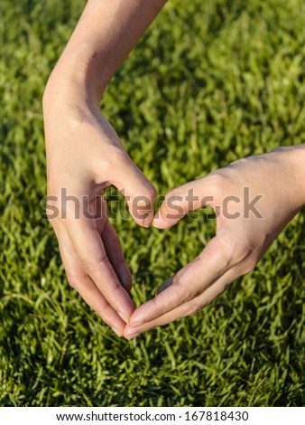 young girl hand make sign of heart by hand on yellow tone grass background