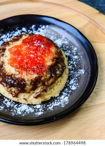 single yellow butter cake with jam and chocolate cream on black dish at old wood background