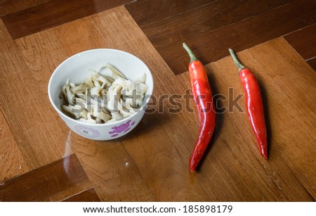 white small mushroom fried with oil in bowl and pepper on brown parquet background