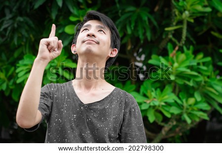 Young asian man pointing with finger to high tree at outdoor natural background