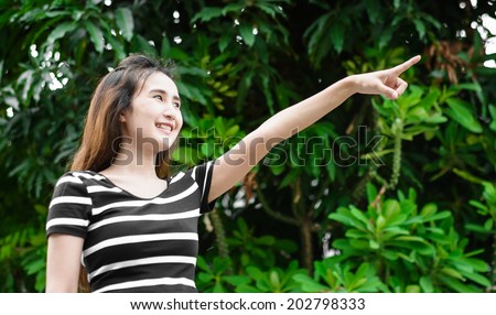 Young asian woman pointing with finger to high tree at outdoor natural background