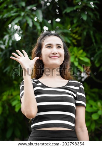happy asia young female greeting and showing her hand up at natural outdoor background