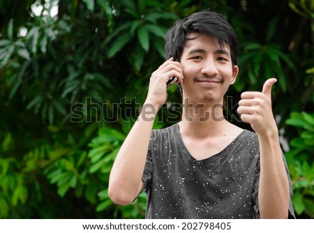 happy Young asia man using and talk smartphone with thumb up at outdoor natural background