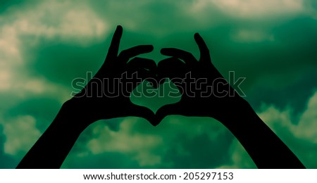 silhouette Girl hand in heart form love sign on sky with retro filter