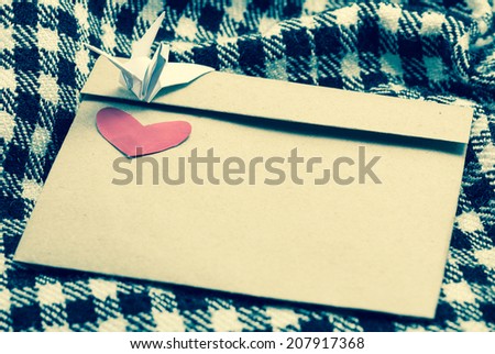 letter envelope with red heart and paper bird at plaid fabric background with retro filter