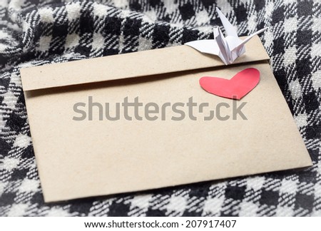 letter brown paper envelope with red heart and paper bird at plaid fabric background