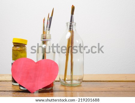 old Brush paints and color bottle with heart paper on wood table at concrete wall