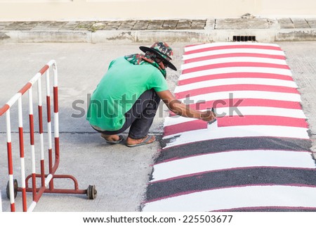 worker using brush for painting white line on the road for caution to reduce the car speed