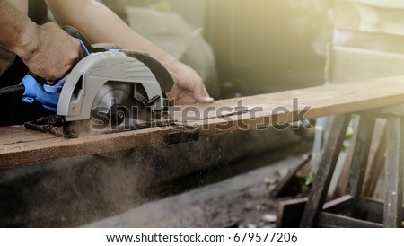 Carpenter using circular saw for cutting wooden boards with power tools.