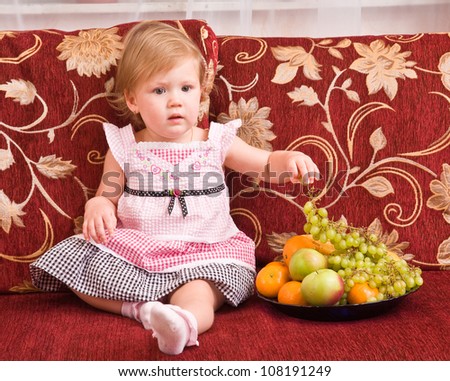 little girl sits on a sofa and eats fruit