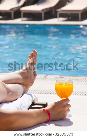 Glass with orange juice on the brink of pool