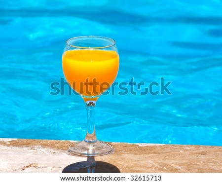 Glass with orange juice on the brink of pool
