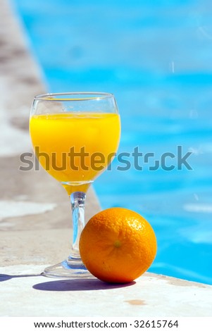 Orange and glass with orange juice on the brink of pool