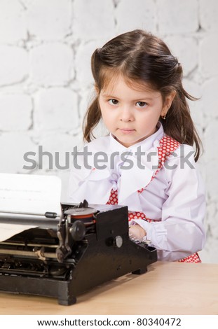 little girl in a white blouse prints on the ancient typewriter