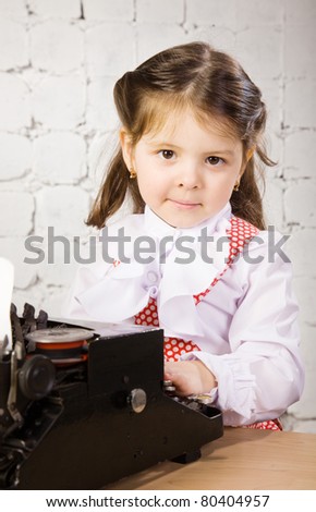 little girl in a white blouse prints on the ancient typewriter
