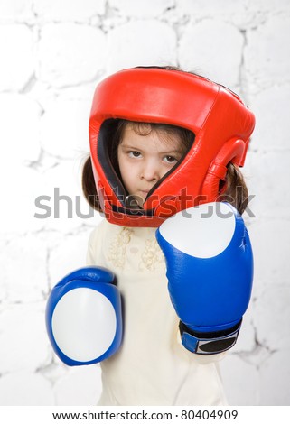 small dark-haired girl in a protective helmet and boxing gloves costs in a fighting rack